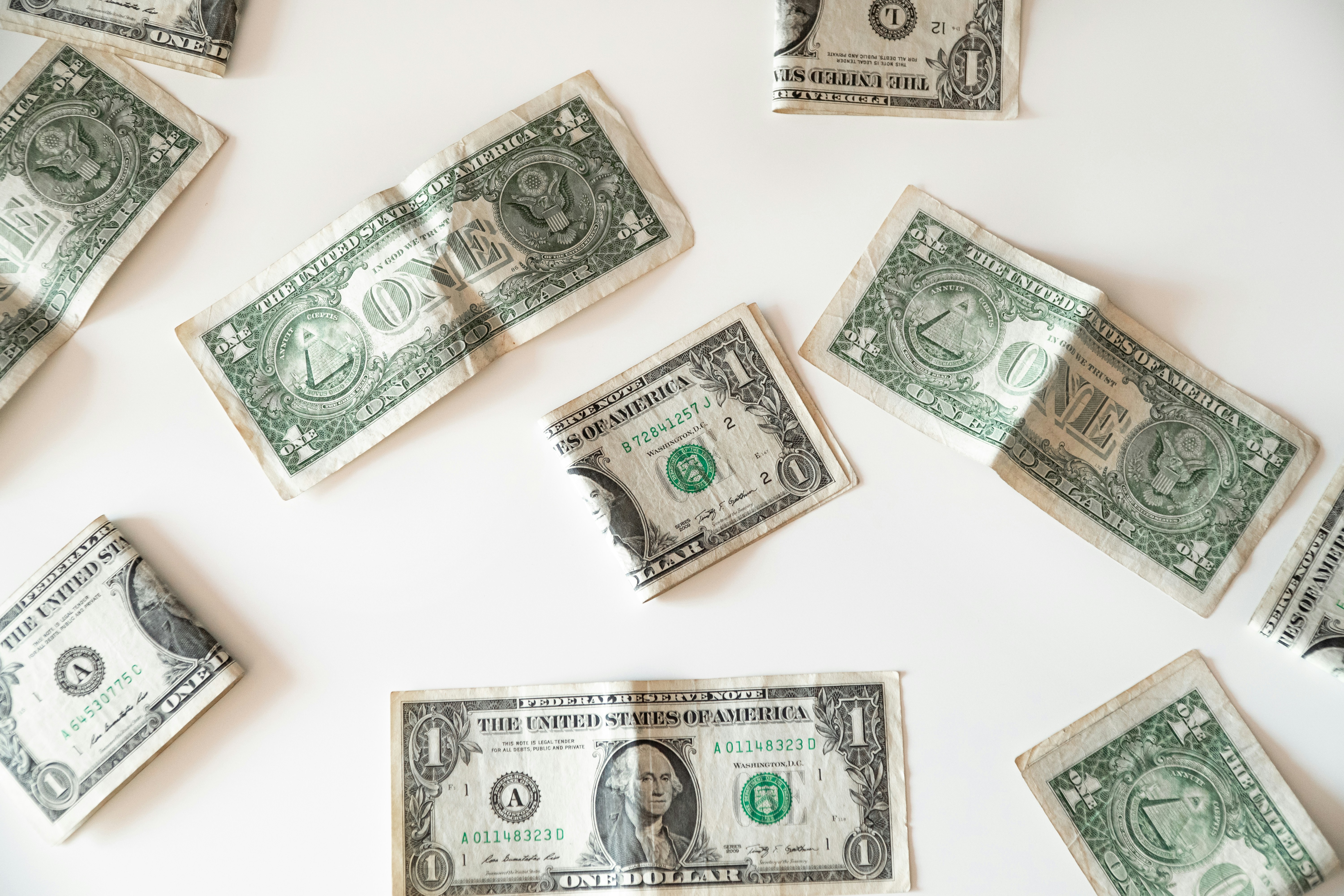 Multiple US dollar bills scattered on white background representing the financial metric a leader cannot defend to stakeholders